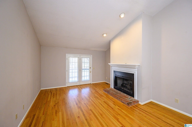 unfurnished living room featuring light wood-style floors, a fireplace with raised hearth, vaulted ceiling, and baseboards