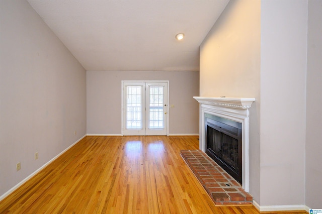 unfurnished living room with a fireplace with raised hearth, baseboards, and wood finished floors