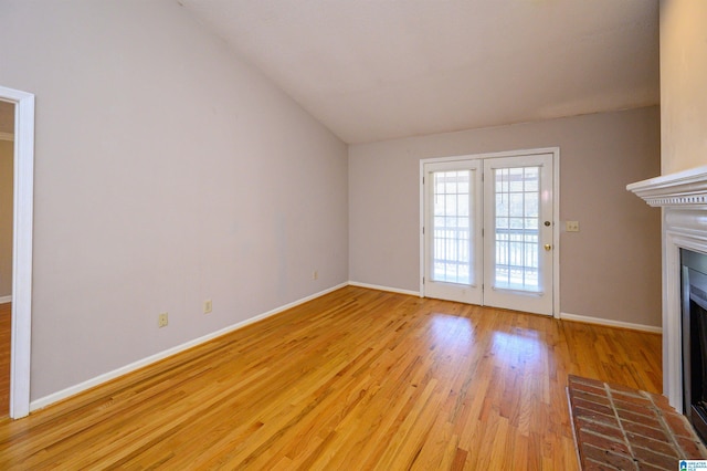 unfurnished living room featuring light wood-type flooring, a fireplace, lofted ceiling, and baseboards