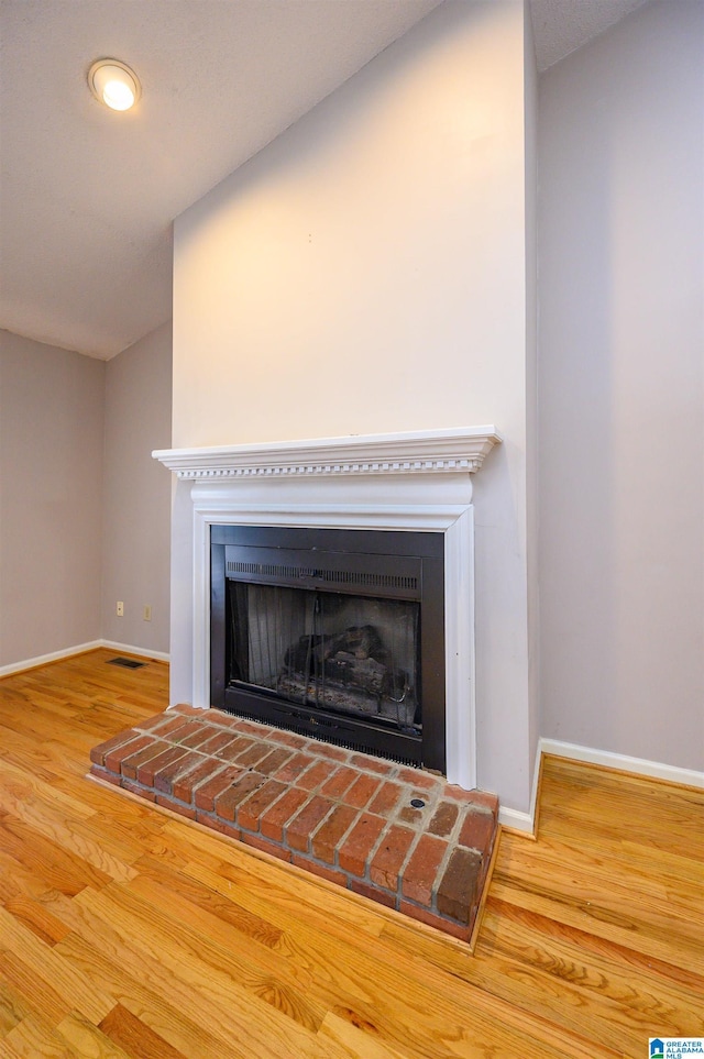 details with a fireplace with raised hearth, wood finished floors, visible vents, and baseboards