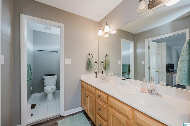 full bath featuring toilet, a sink, baseboards, and double vanity