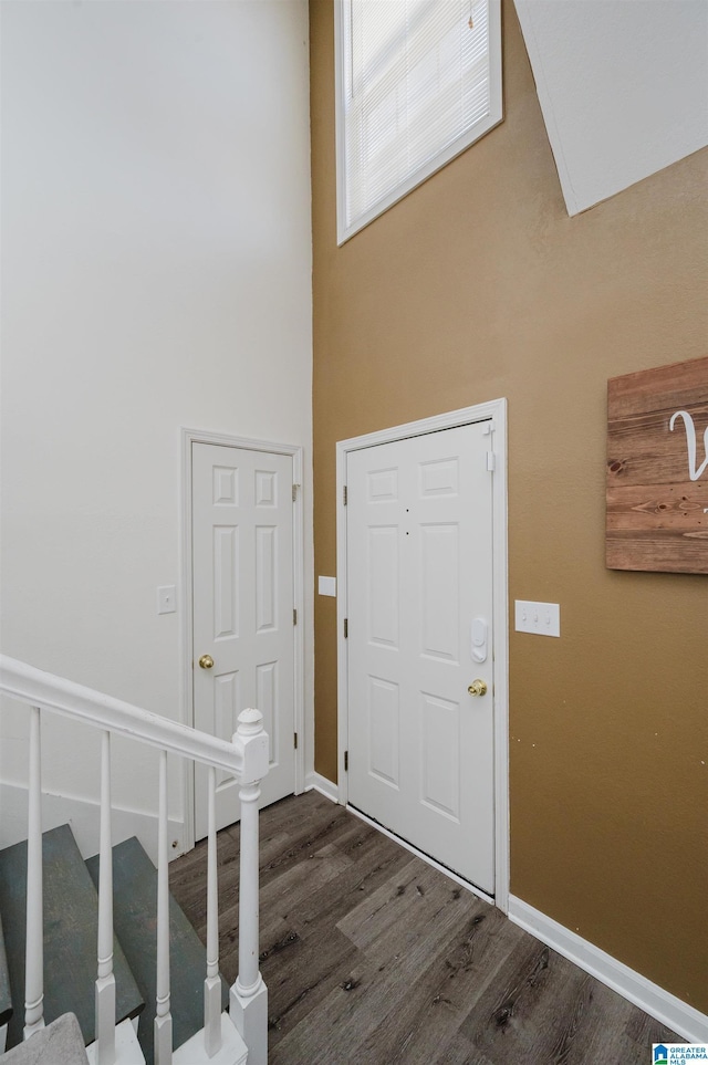 entryway with dark wood-type flooring, a towering ceiling, stairway, and baseboards