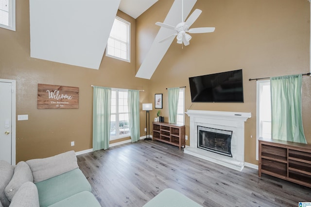 living area with a fireplace with raised hearth, a high ceiling, ceiling fan, wood finished floors, and baseboards