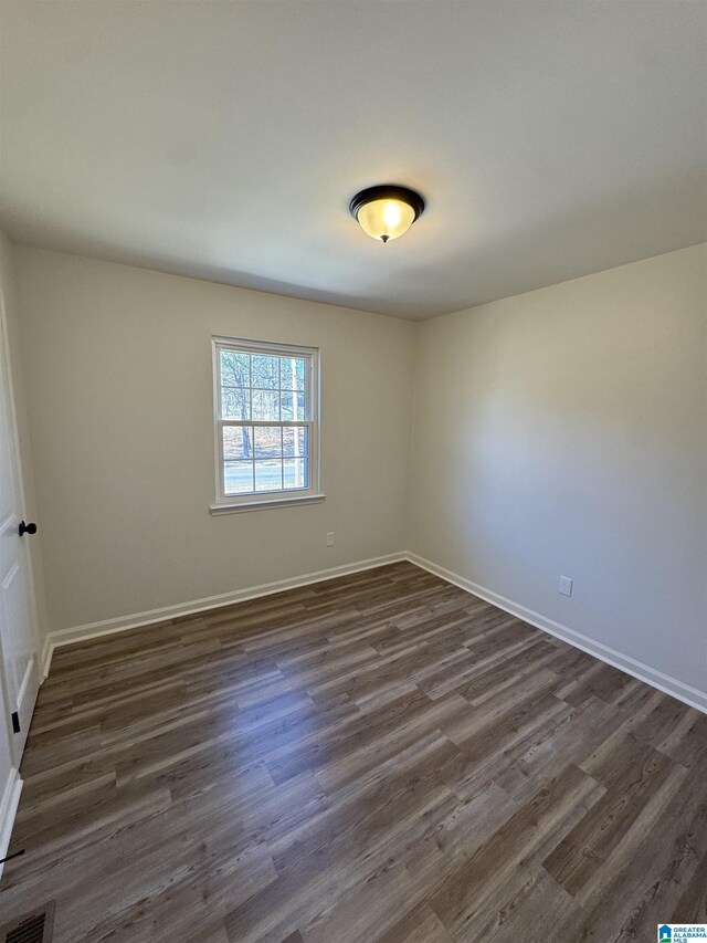 empty room featuring dark wood-type flooring, visible vents, and baseboards