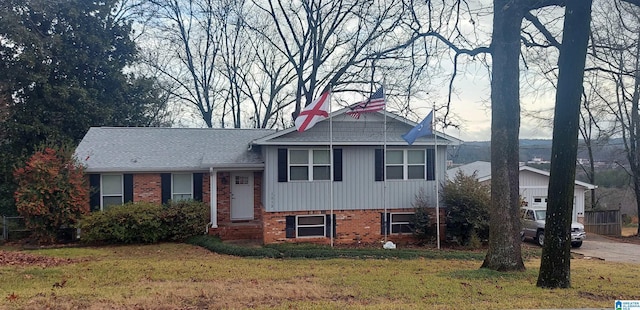 split level home featuring brick siding, a front lawn, and roof with shingles