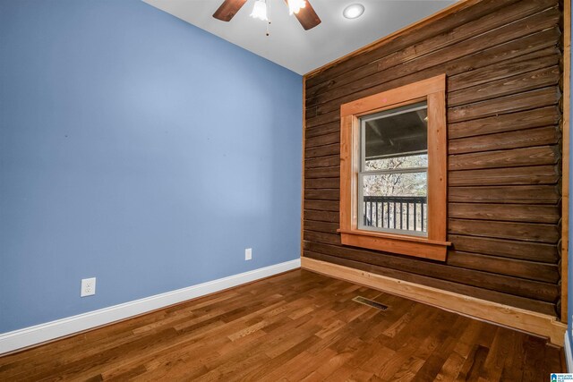 spare room with baseboards, visible vents, dark wood finished floors, a ceiling fan, and wood walls