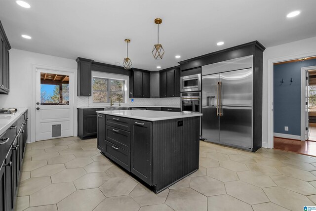 kitchen with built in appliances, light countertops, dark cabinetry, a center island, and tasteful backsplash