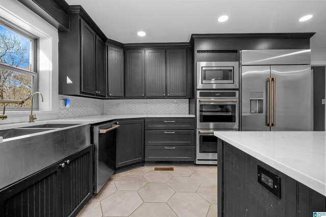 kitchen with light tile patterned floors, tasteful backsplash, appliances with stainless steel finishes, dark cabinets, and light countertops