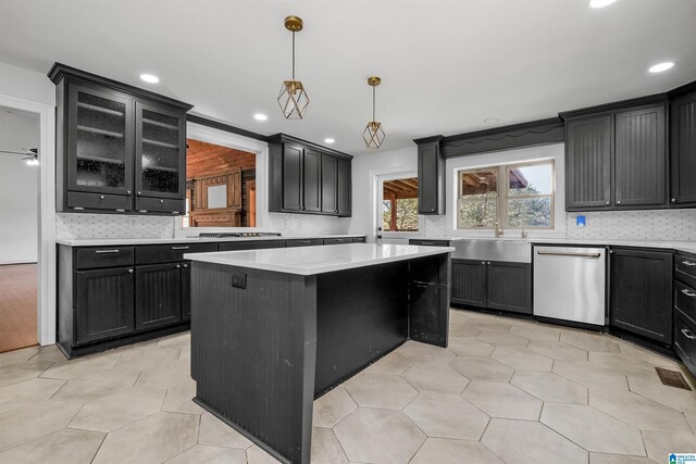 kitchen featuring light countertops, decorative backsplash, a kitchen island, dark cabinetry, and dishwasher