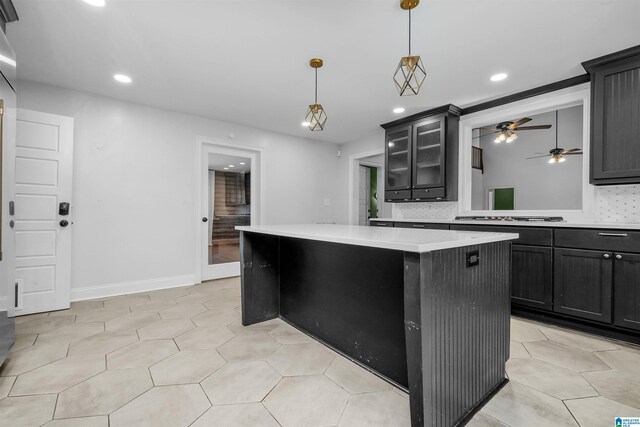 kitchen with decorative backsplash, a center island, light countertops, dark cabinetry, and stainless steel gas cooktop