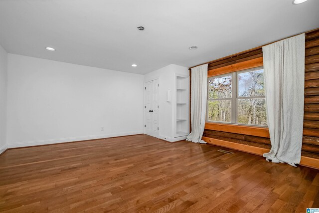 empty room featuring recessed lighting, rustic walls, baseboards, and wood finished floors