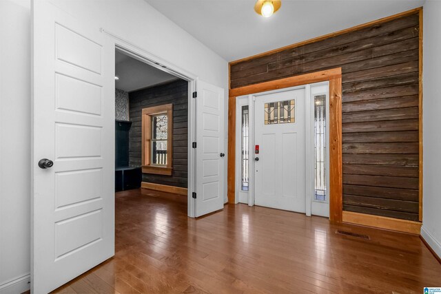 foyer with wood walls, wood-type flooring, visible vents, and baseboards