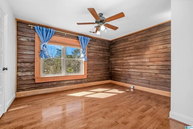 empty room with wooden walls, wood finished floors, a ceiling fan, and baseboards