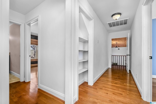 corridor featuring light wood-type flooring, an upstairs landing, visible vents, and baseboards