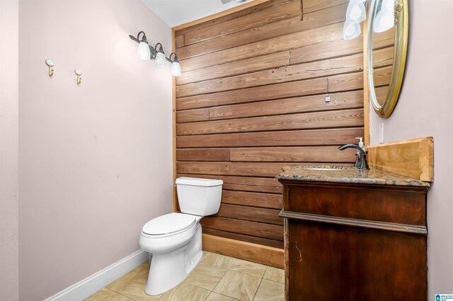 half bathroom featuring baseboards, wood walls, vanity, and toilet