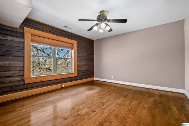 empty room with baseboards, wooden walls, visible vents, and wood finished floors