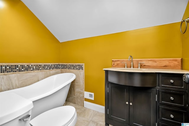 bathroom featuring visible vents, toilet, a soaking tub, vaulted ceiling, and vanity