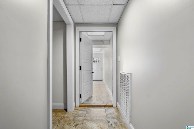 corridor with baseboards, visible vents, and a drop ceiling