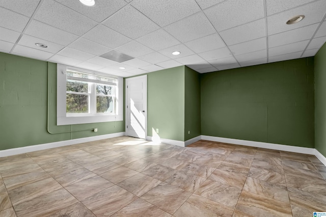 unfurnished room featuring concrete block wall, baseboards, a drop ceiling, and recessed lighting