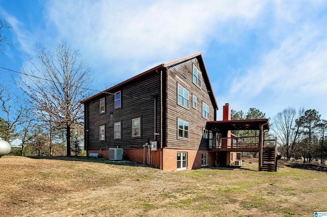 back of house with central AC unit, stairway, a chimney, and a lawn