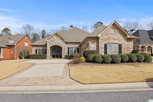 view of front facade with driveway, brick siding, roof with shingles, and a front yard