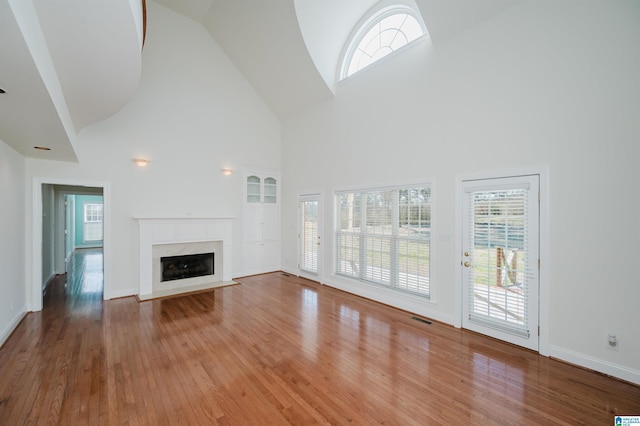 unfurnished living room featuring high vaulted ceiling, a fireplace, wood finished floors, visible vents, and baseboards