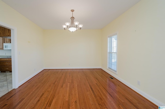 empty room featuring an inviting chandelier, visible vents, baseboards, and wood finished floors