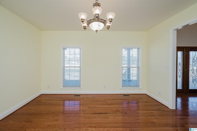 spare room with a notable chandelier, baseboards, a wealth of natural light, and wood finished floors