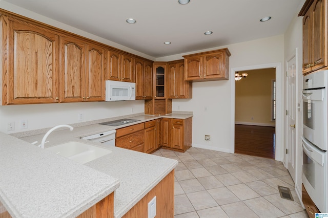 kitchen featuring a peninsula, white appliances, a sink, light countertops, and brown cabinets