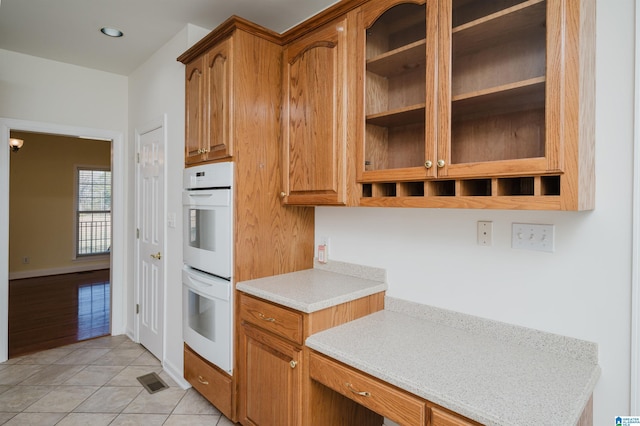 kitchen with light tile patterned floors, recessed lighting, light countertops, double oven, and brown cabinetry