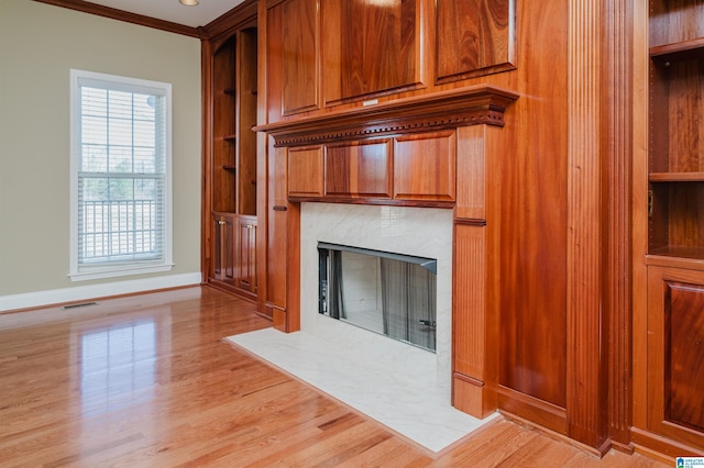 unfurnished living room with crown molding, visible vents, a fireplace, and light wood finished floors