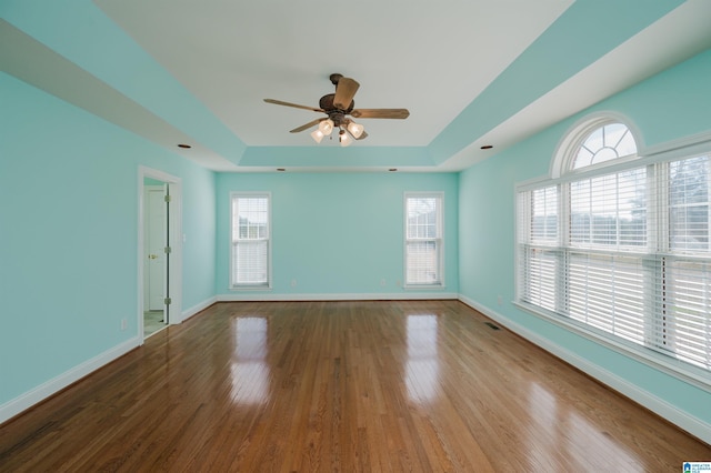 unfurnished room featuring a ceiling fan, baseboards, a raised ceiling, and wood finished floors