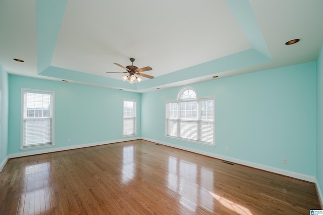 spare room featuring a healthy amount of sunlight, visible vents, a raised ceiling, and hardwood / wood-style floors