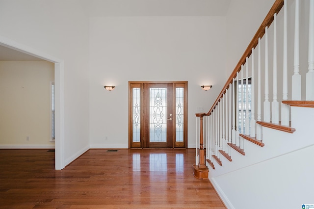 foyer with stairway, wood finished floors, a towering ceiling, and baseboards