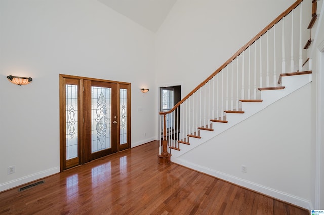 foyer entrance featuring baseboards, visible vents, a towering ceiling, wood finished floors, and stairs