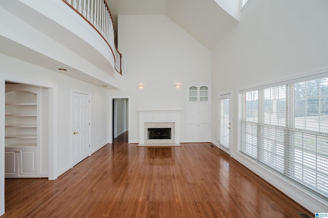 unfurnished living room with built in shelves, wood finished floors, and a healthy amount of sunlight