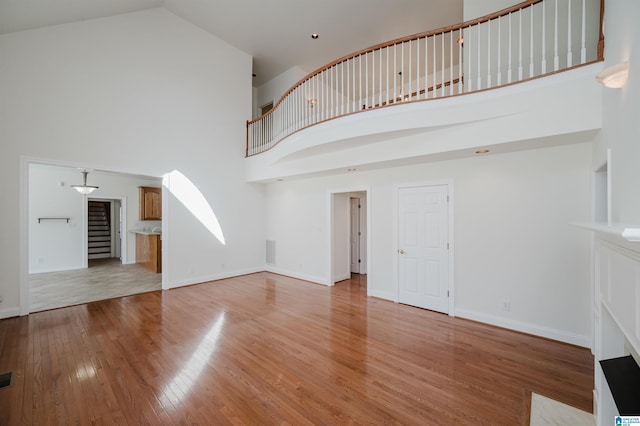 unfurnished living room featuring visible vents, a towering ceiling, light wood-style floors, baseboards, and stairs