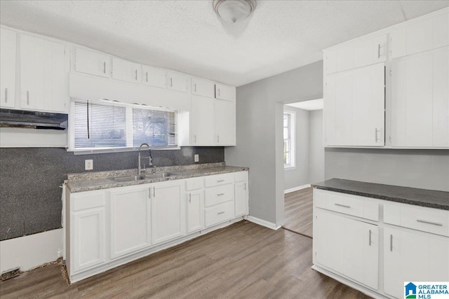 kitchen with white cabinets, a sink, a textured ceiling, wood finished floors, and baseboards