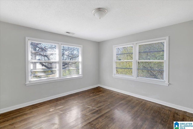 unfurnished room with a textured ceiling, dark wood-type flooring, visible vents, and baseboards