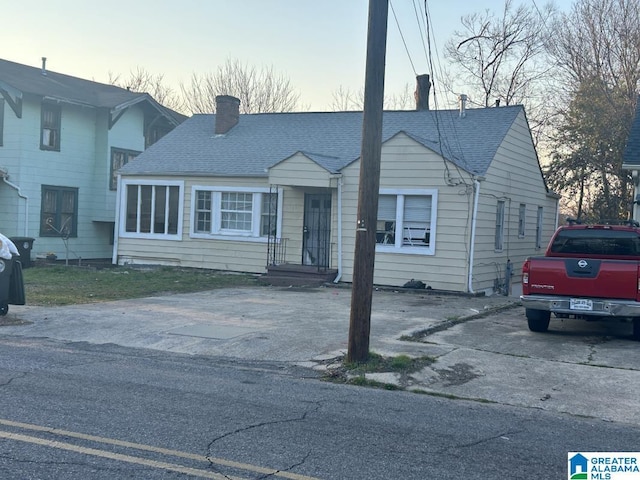 view of front of house with driveway, a chimney, and roof with shingles