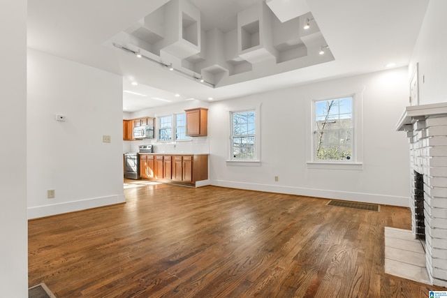 unfurnished living room featuring plenty of natural light, a brick fireplace, wood finished floors, and baseboards