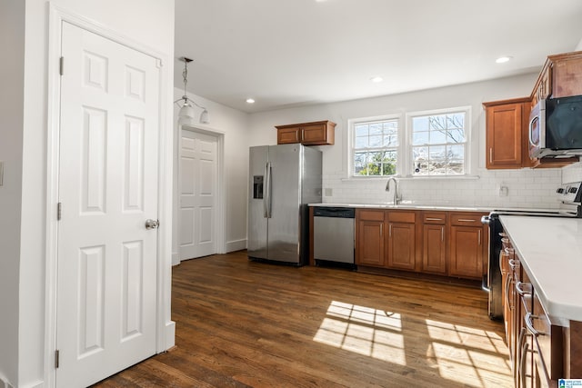 kitchen with brown cabinetry, dark wood-style flooring, stainless steel appliances, and a sink