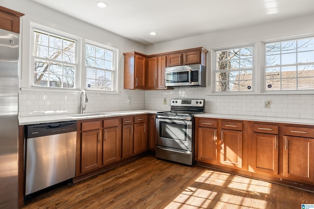 kitchen with dark wood-style floors, a sink, stainless steel appliances, light countertops, and backsplash