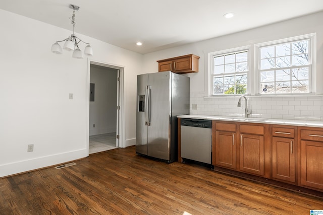 kitchen with stainless steel appliances, a sink, light countertops, backsplash, and brown cabinets