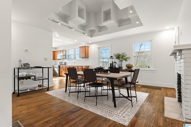 dining room with a fireplace, wood finished floors, a wealth of natural light, and baseboards