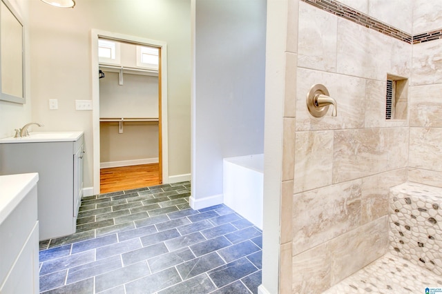 bathroom featuring tiled shower, a walk in closet, vanity, and baseboards