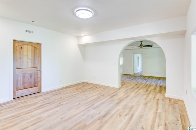 unfurnished room featuring arched walkways, light wood finished floors, visible vents, a ceiling fan, and baseboards