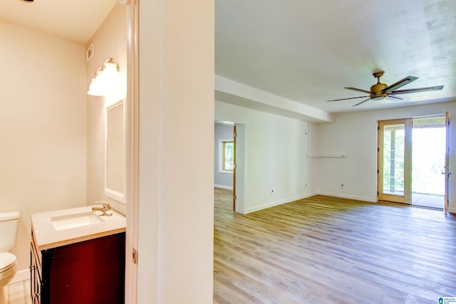 half bath featuring toilet, wood finished floors, vanity, baseboards, and a ceiling fan