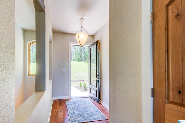 foyer entrance featuring visible vents, a textured wall, baseboards, and wood finished floors