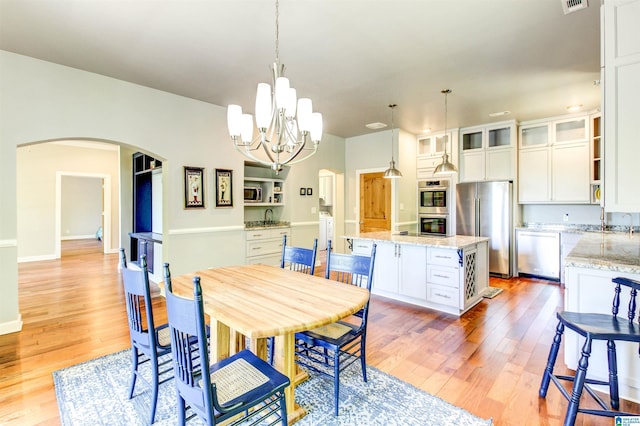 dining room featuring arched walkways, an inviting chandelier, light wood-style floors, washer / dryer, and baseboards